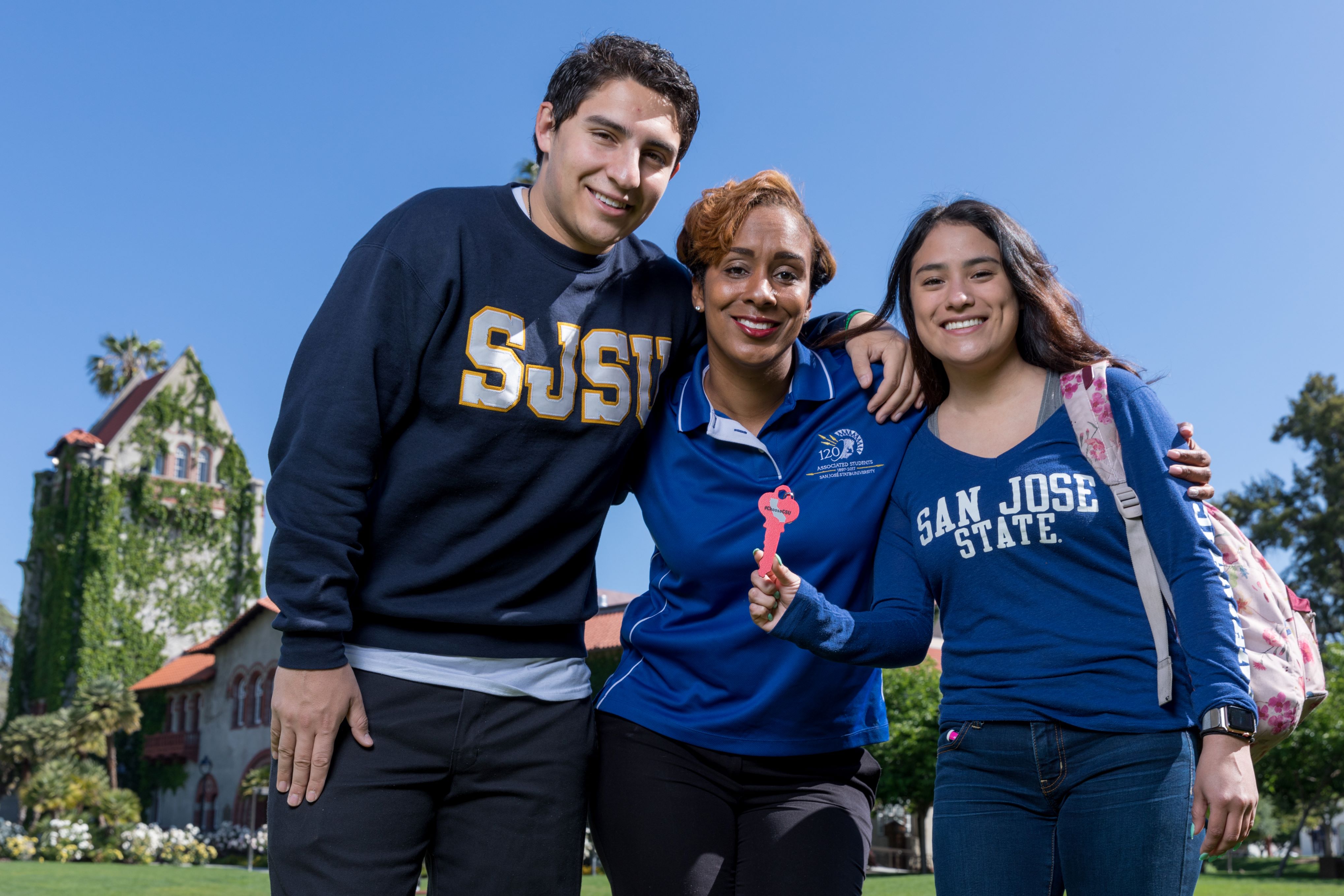Three people hug posing outside on a sunny day
