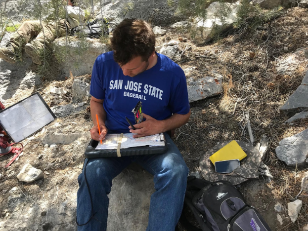 A student sits in the shade of a juniper to record his data on his geologic map.