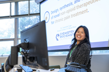 student presents with computer in foreground and presentation screen in back